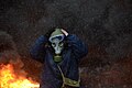 Protester wearing a tear gas mask against background of the massive fire set by protesters to prevent internal forces from crossing the barricade line. Kyiv, Ukraine. Jan 22, 2014