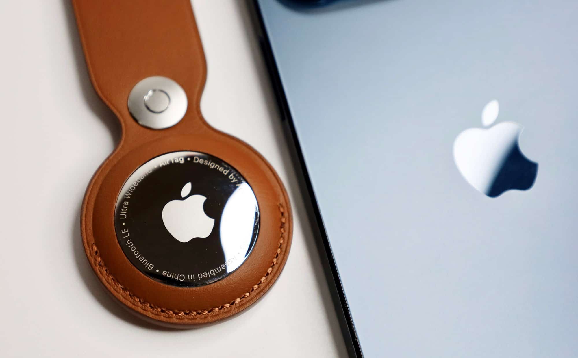 Apple Airtag in keychain holder lying beside Apple iPhone