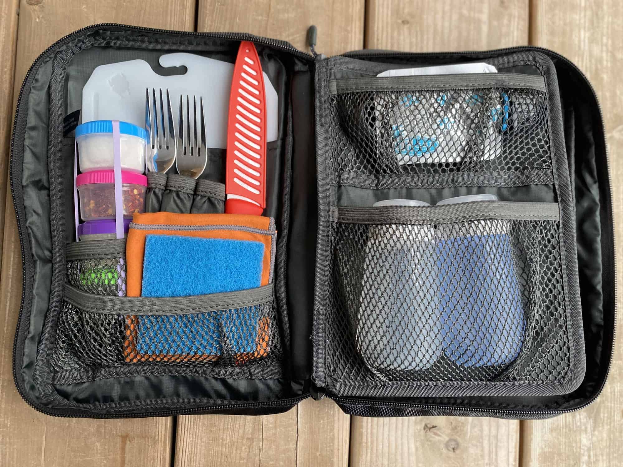 Travel cooking gadget kit on a wooden table, with a range of cutlery, containers, and other kitchen items